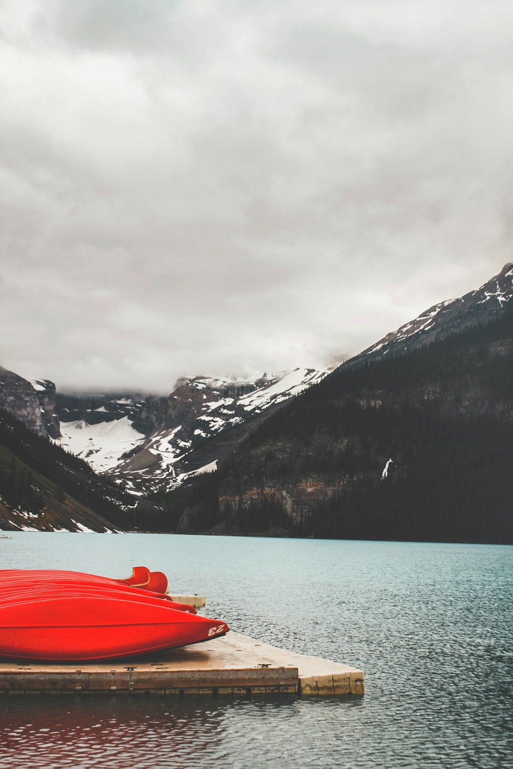 red kayak on lake near snow covered mountain during daytime