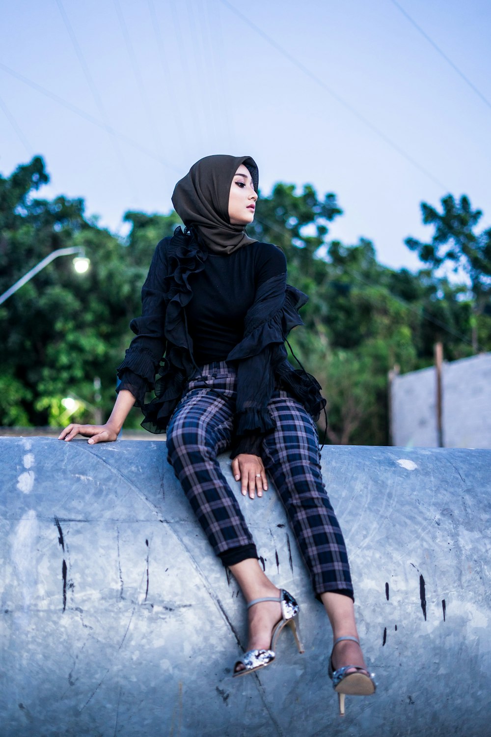 donna in hijab nero e pantaloni a quadri bianchi e neri seduta su una panchina di cemento durante il giorno