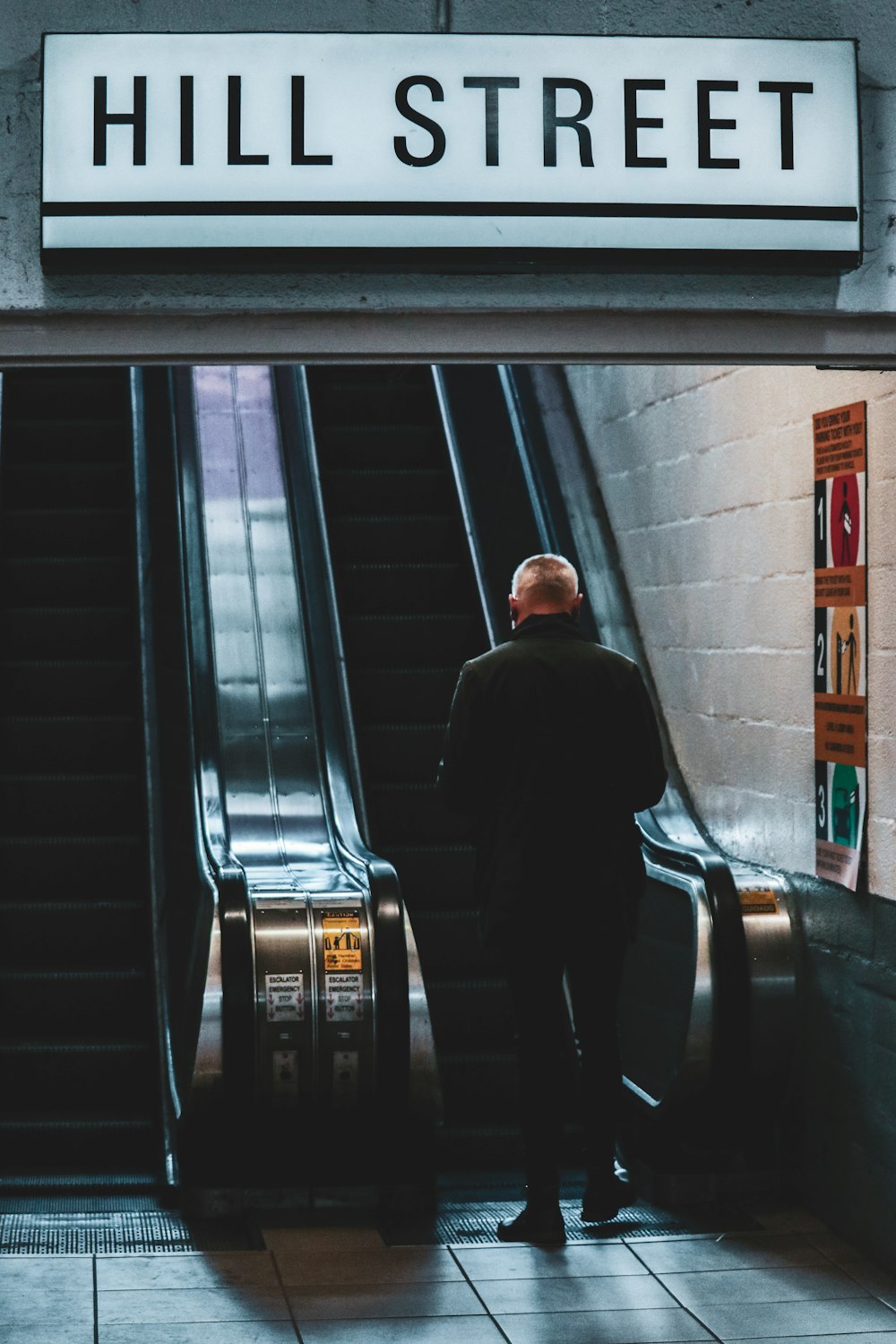 Mann in schwarzer Jacke steht auf Rolltreppe