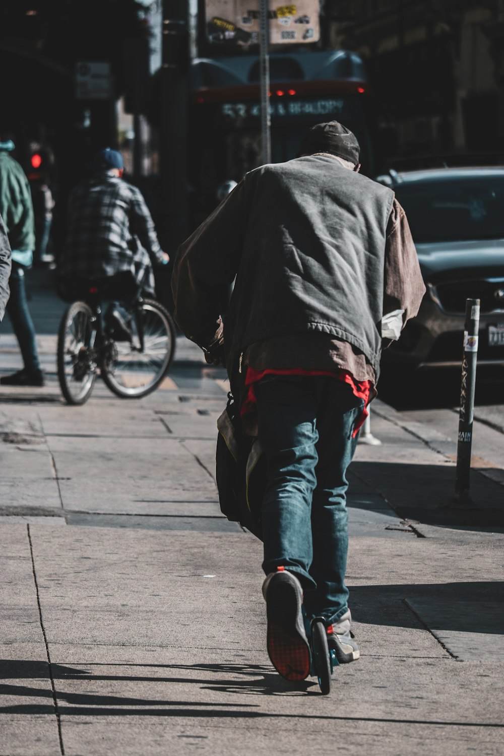 uomo in giacca nera e jeans blu denim che cammina sul marciapiede durante il giorno