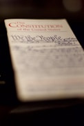 A close-up shot of a document titled 'The Constitution of the United States'. The words 'We the People' are prominently in view, with cursive handwriting below.