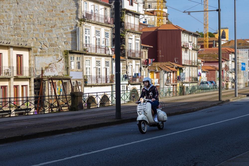 Mann in schwarzer Jacke fährt tagsüber mit weißem Motorroller auf der Straße