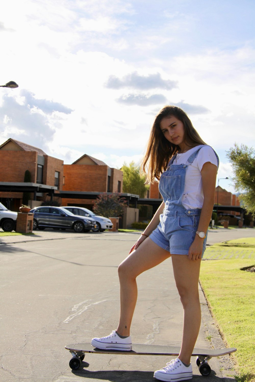 woman in white t-shirt and blue denim shorts standing on gray concrete pavement during daytime