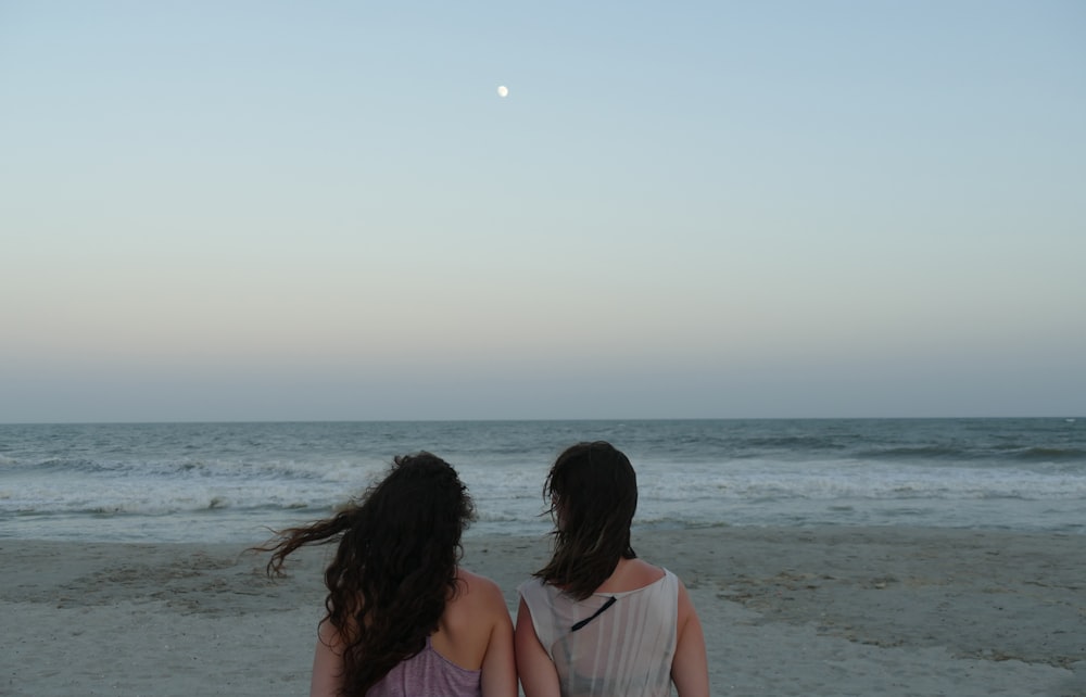 2 women in white tank top sitting on beach during daytime