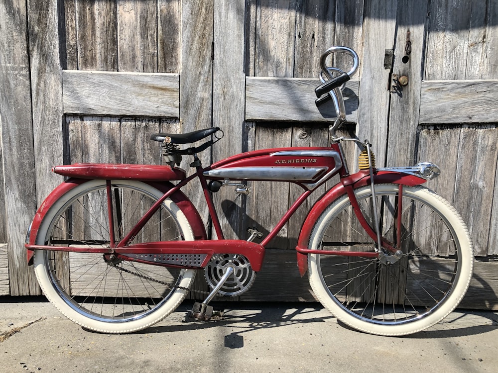 Bicicleta roja de la ciudad apoyada en la pared de madera marrón