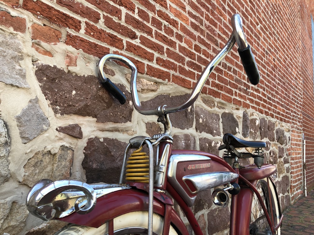 red and silver bicycle beside brown brick wall