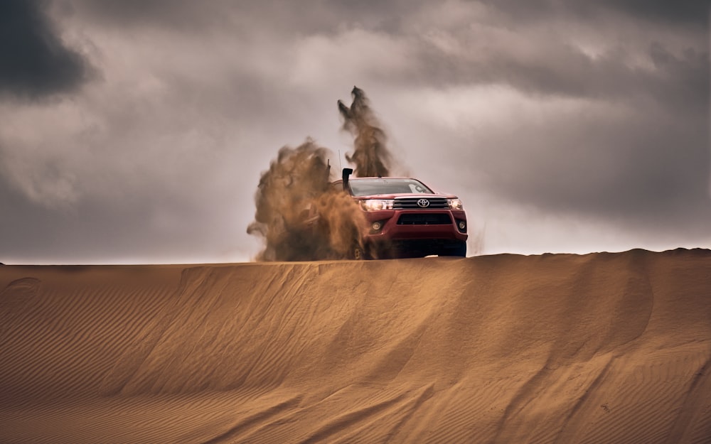 red suv on desert under gray clouds