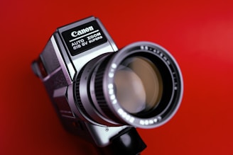 A vintage Canon Super 8 movie camera with a large, prominent lens and detailed labels set against a bold red background.