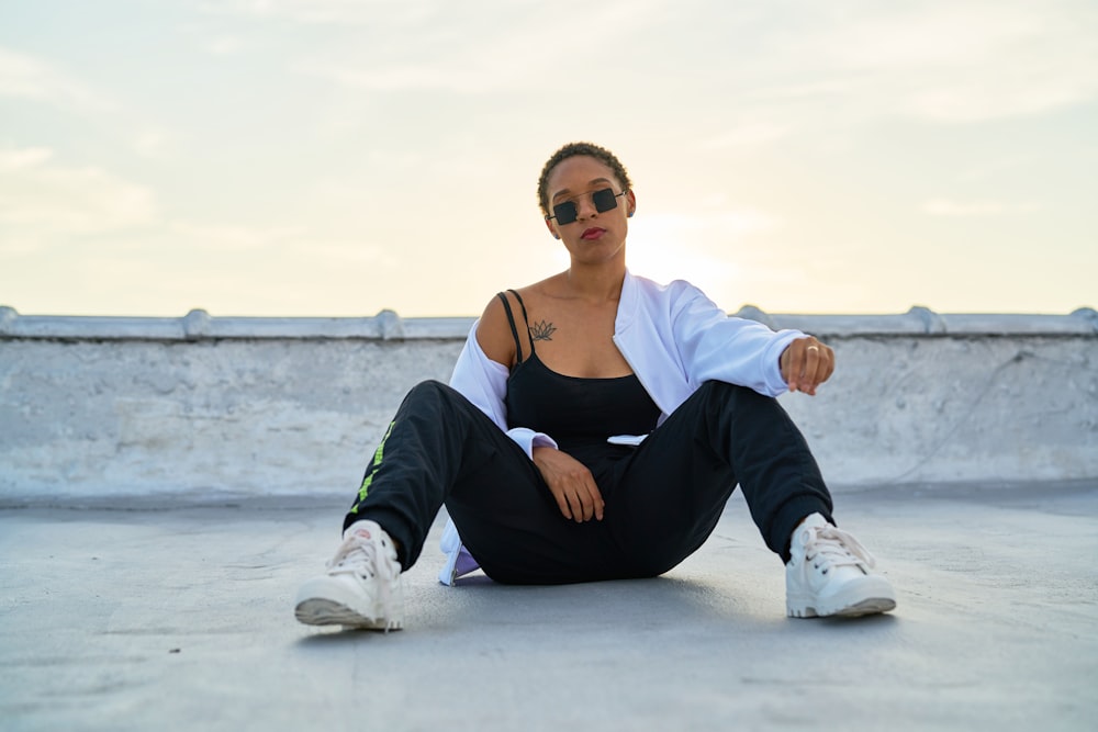 woman in black tank top and black pants sitting on white sand during daytime