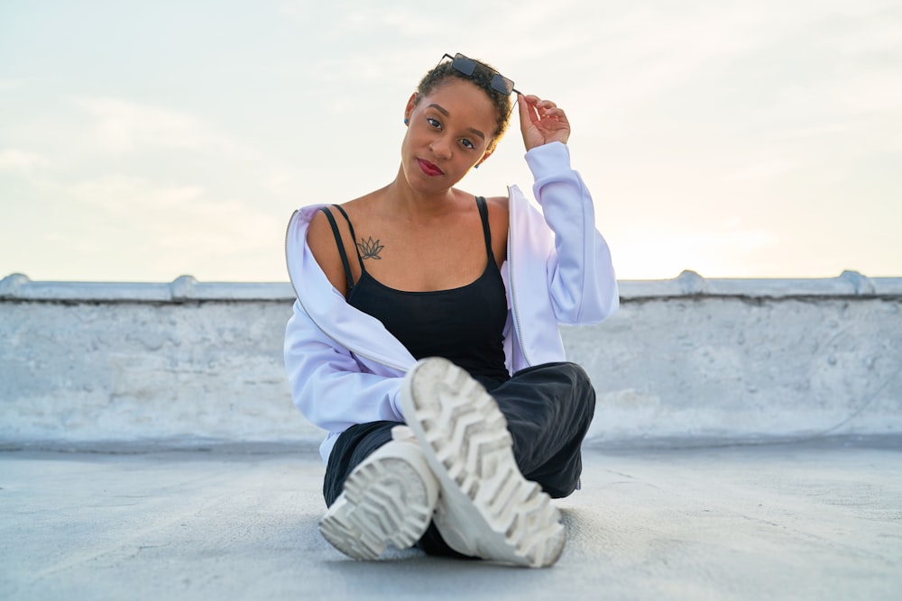 woman in black tank top and white cardigan sitting on white sand during daytime