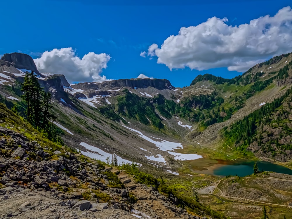 lake in the middle of mountains under blue sky and white clouds during daytime