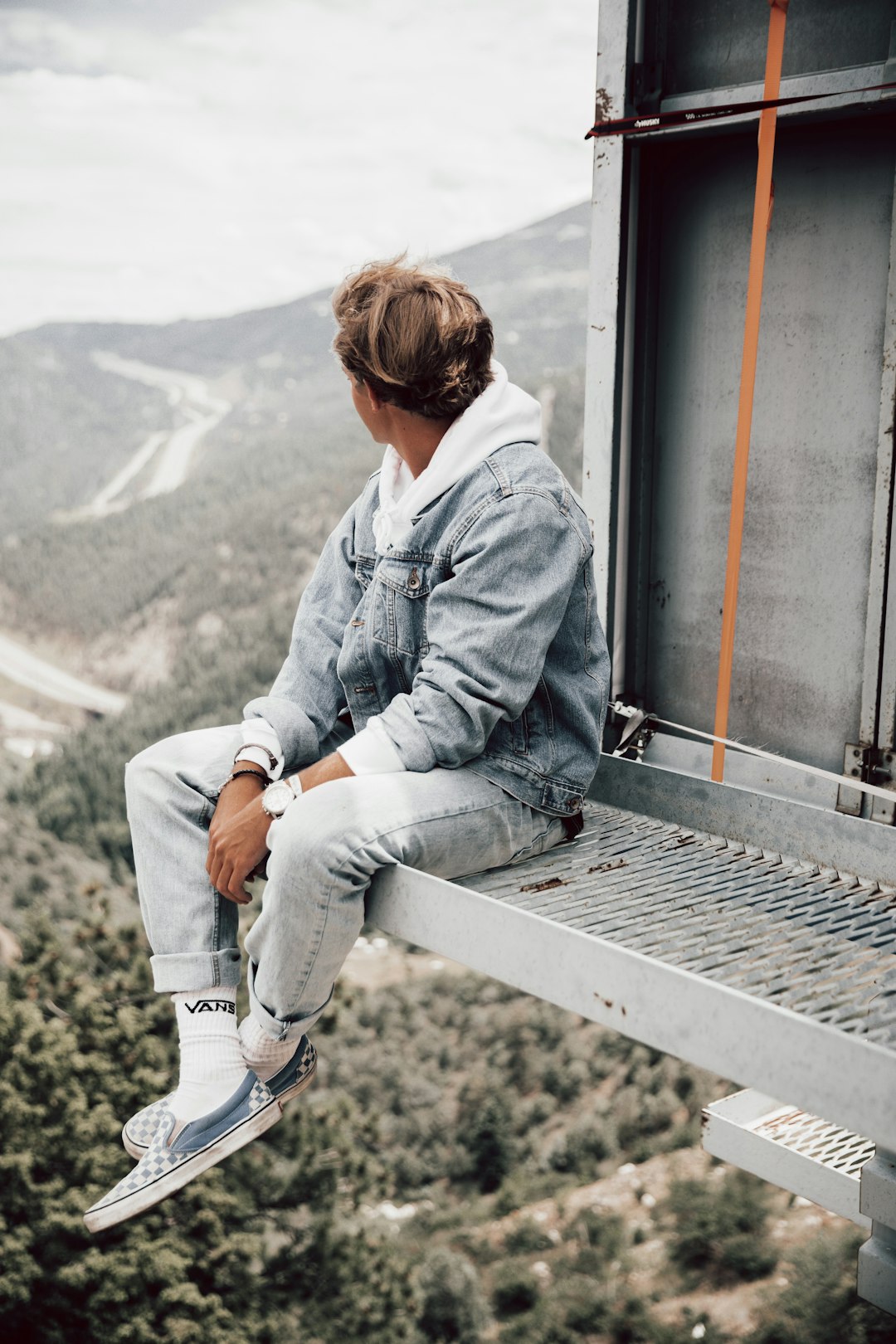 man in blue denim jacket sitting on train rail during daytime