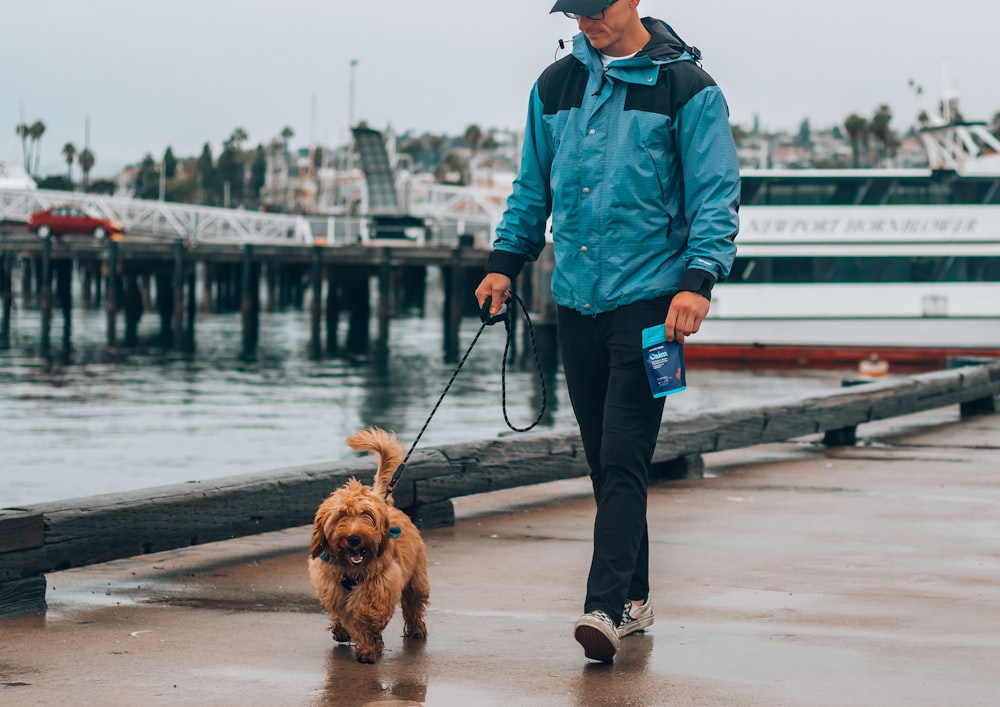 man in blue jacket and black pants standing beside brown long coated dog on dock during