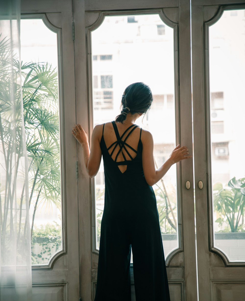 Mujer con camiseta sin mangas negra y roja de pie cerca de una ventana de vidrio con marco de madera blanca