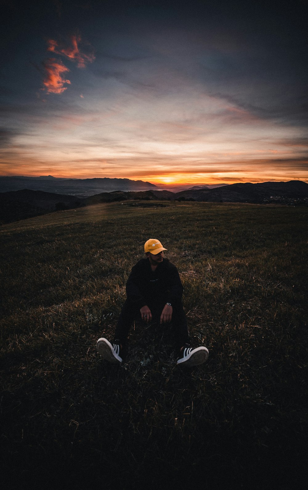 man in black jacket sitting on green grass field during sunset