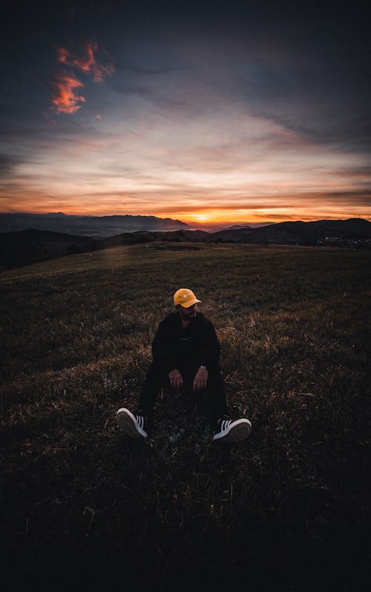 man in black jacket sitting on green grass field during sunset in Miliana Algeria