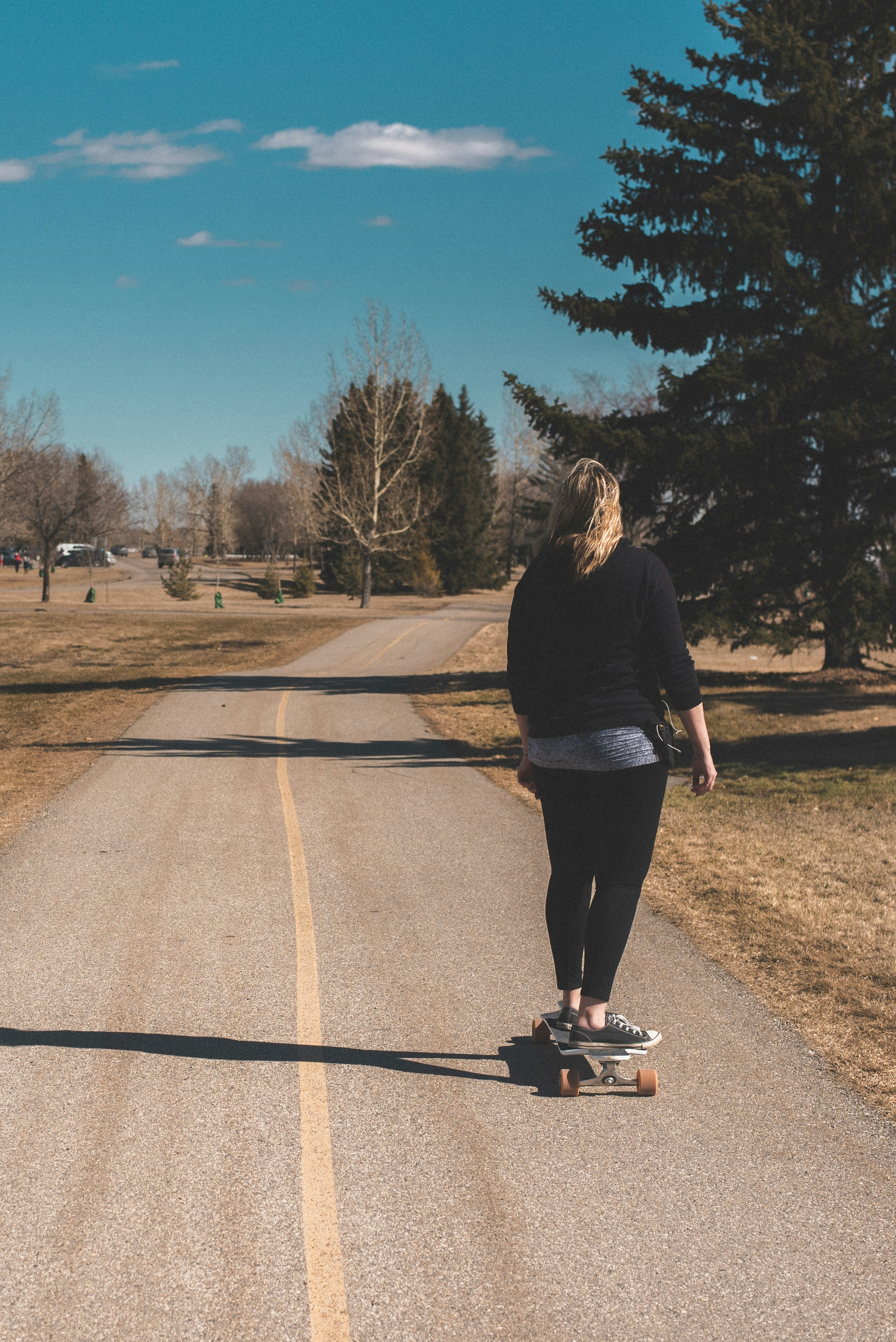 woman in black long sleeve shirt and black pants standing on brown asphalt road during daytime