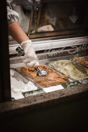A smiling delivery person handing over a box of assorted artisanal gelato tubs to a café owner.