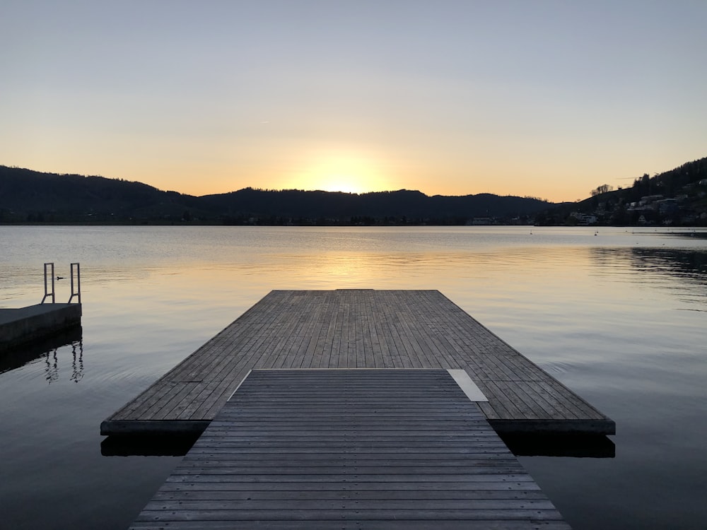 Muelle de madera marrón en el cuerpo de agua durante la puesta del sol