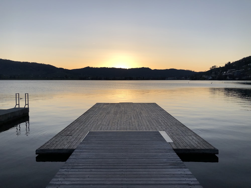 brown wooden dock on body of water during sunset