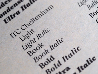 A close-up of a printed page displaying various font styles and weights including Light, Light Italic, Book, Book Italic, and Bold. The text is crisp and clear, showcasing different typography samples in black ink on a light gray or beige paper.