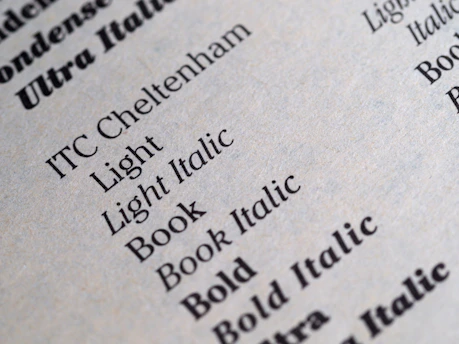 A close-up of a printed page displaying various font styles and weights including Light, Light Italic, Book, Book Italic, and Bold. The text is crisp and clear, showcasing different typography samples in black ink on a light gray or beige paper.
