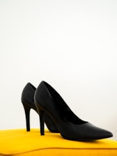 A stylish pair of black and gold high-heeled shoes displayed against a minimalist white background.