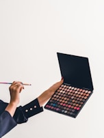 Hands holding a delicate makeup brush over a palette of vibrant eyeshadows.
