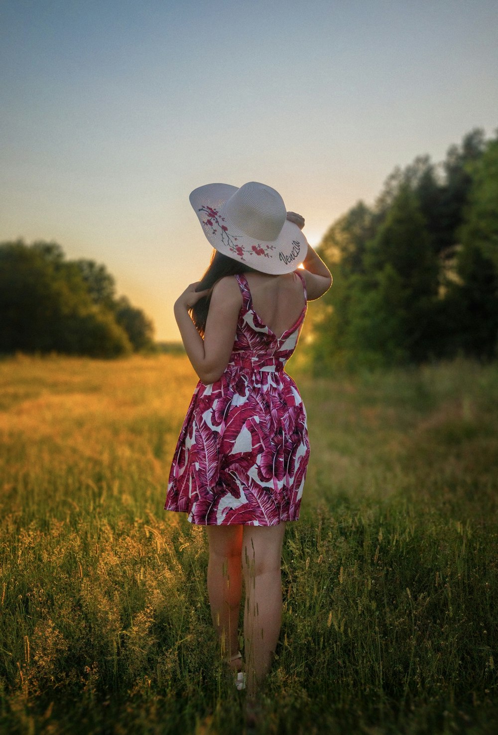 白い日よけ帽をかぶった白と紫の花柄のドレスを着た女性が緑の草原に立っています