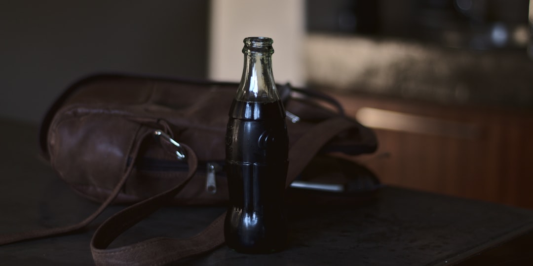 black glass bottle beside black framed eyeglasses on brown wooden table