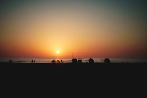 Sunset over Ipanema beach with colorful skies and silhouettes of people enjoying the shore.