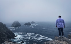 person in blue jacket standing on rock formation near body of water during daytime