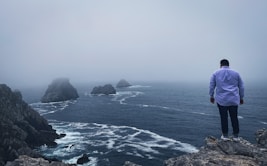 person in blue jacket standing on rock formation near body of water during daytime
