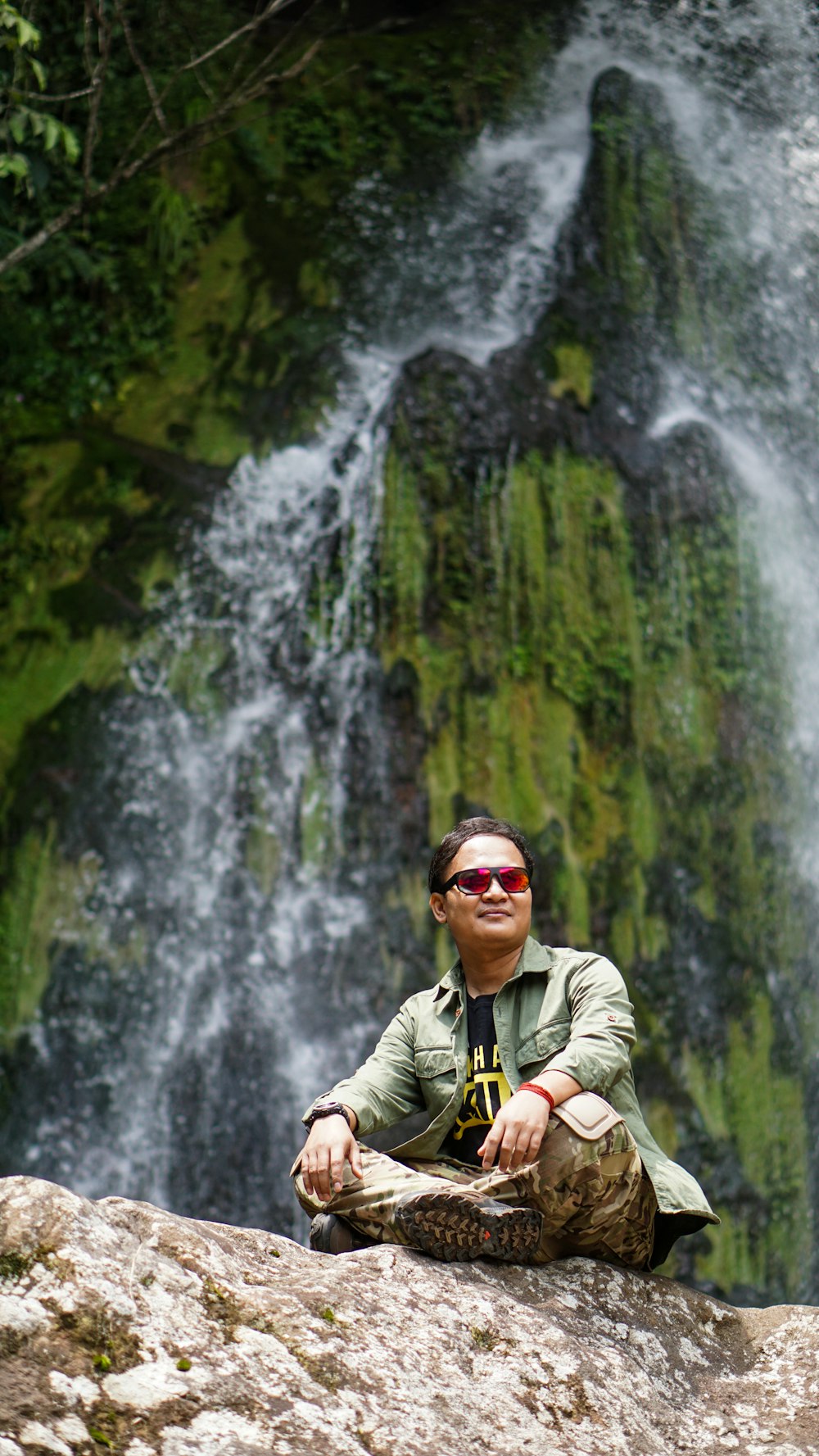 Hombre con chaqueta verde con gafas de sol negras cerca de cascadas durante el día