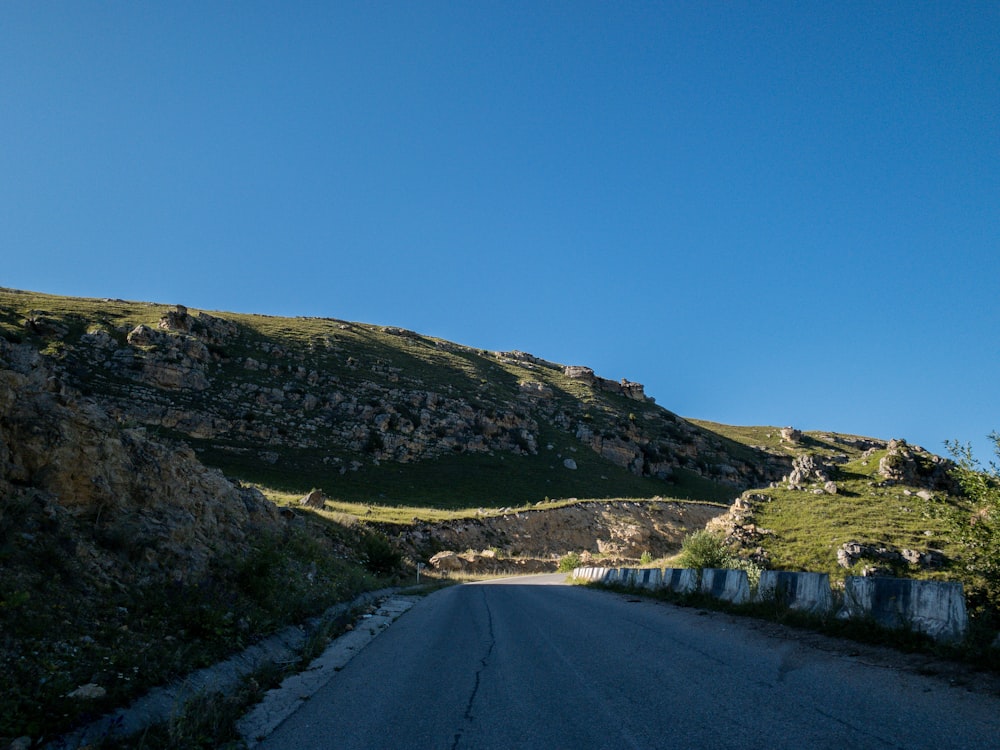 gray road between green grass field under blue sky during daytime