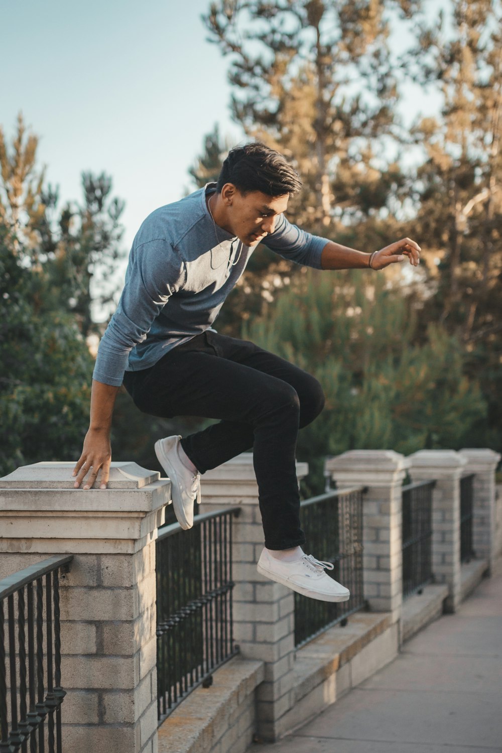 homme en polo à rayures bleues et blanches et pantalon noir assis sur une clôture en béton blanc