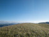 Rolling green hills with wildflowers stretching towards distant peaks.