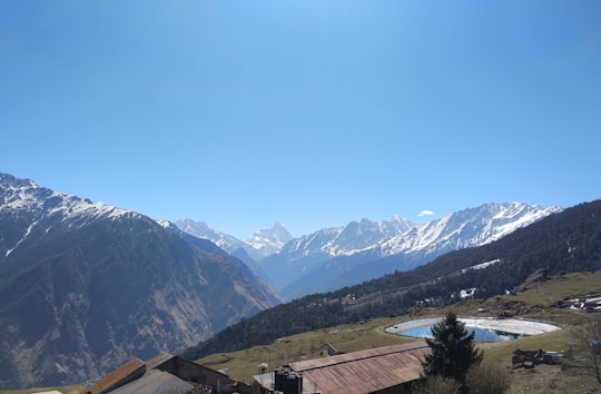brown and white house near green trees and mountains under blue sky during daytime in Auli India