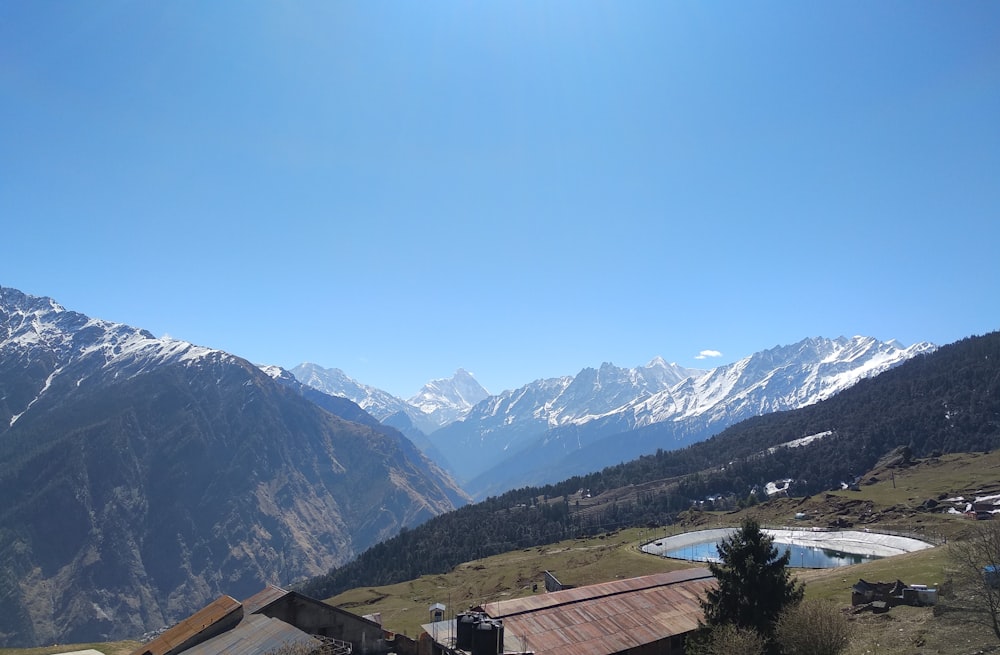 Casa marrone e bianca vicino agli alberi verdi e alle montagne sotto il cielo blu durante il giorno