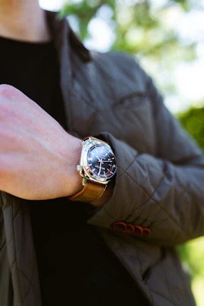 Close-up shot of a hand adjusting a sleek black leather watch against a neutral gray background.