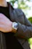 Close-up of a stylish man adjusting his watch, with a blurred city background.