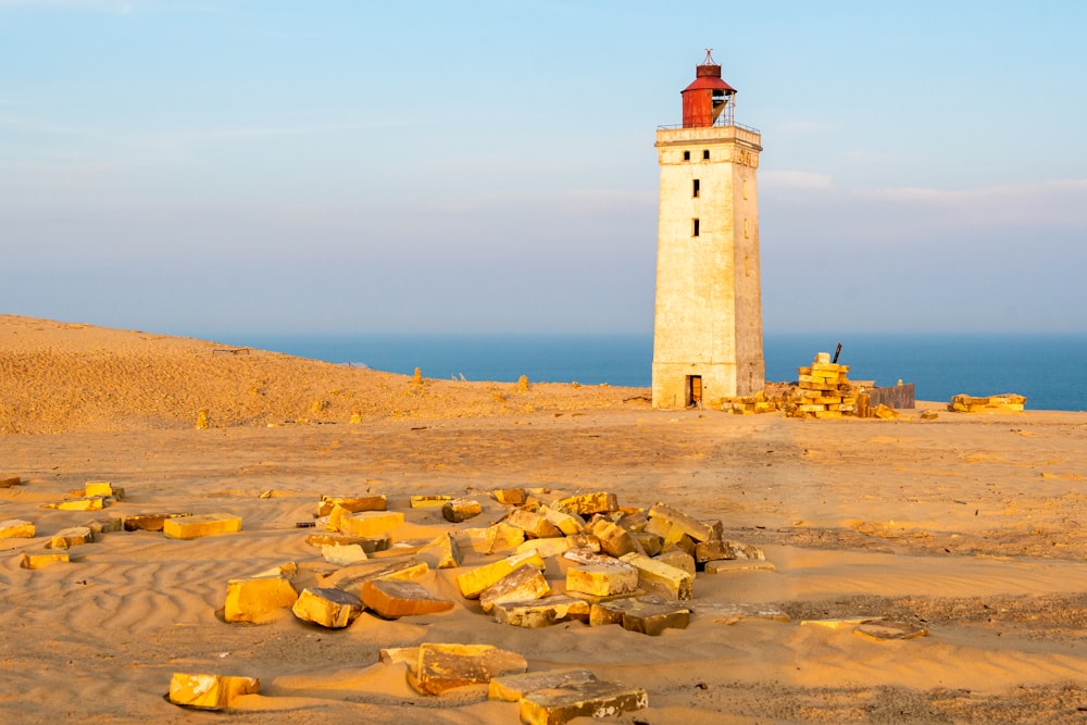 white and brown lighthouse on brown sand near body of water during daytime