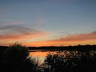 A vibrant oil painting of a serene lakeside at sunset, showcasing warm oranges and cool blues.