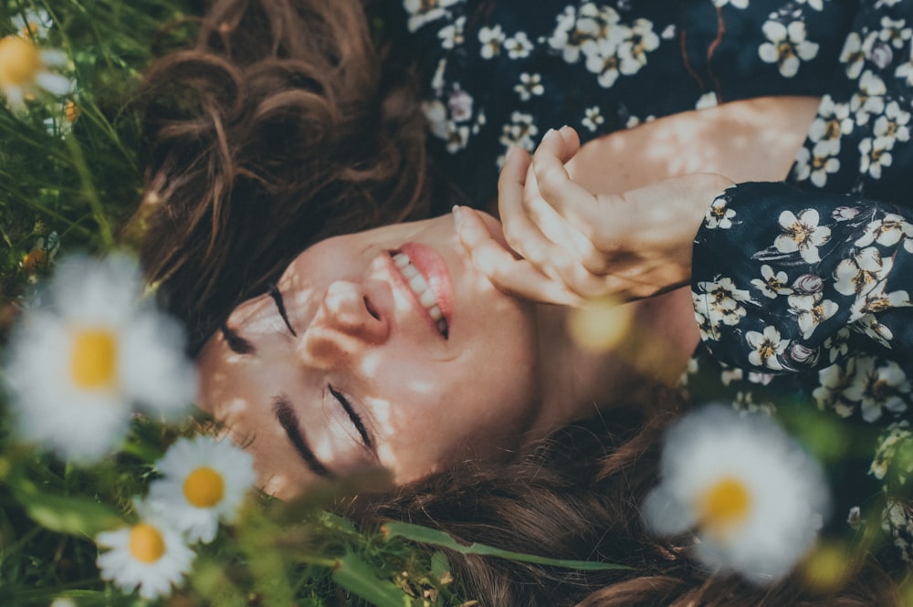 緑の芝生に横たわる黒と白の花柄のシャツを着た女性