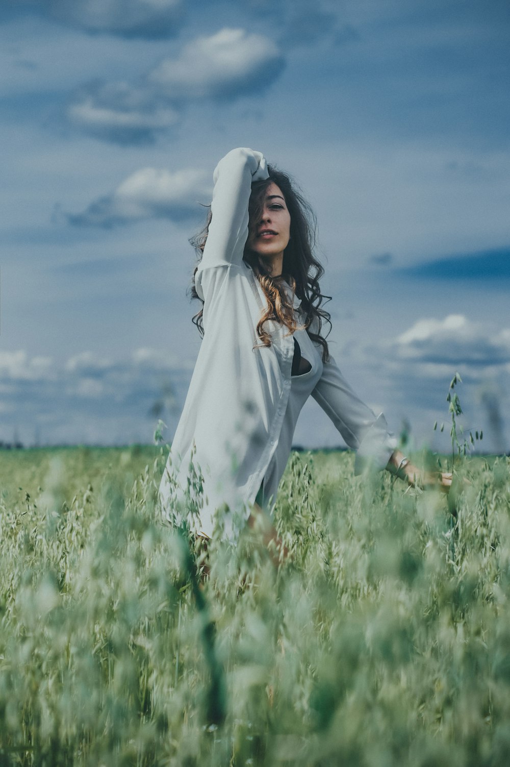 昼間の青空の下の緑の草原に立つ白い長袖ドレスの女性