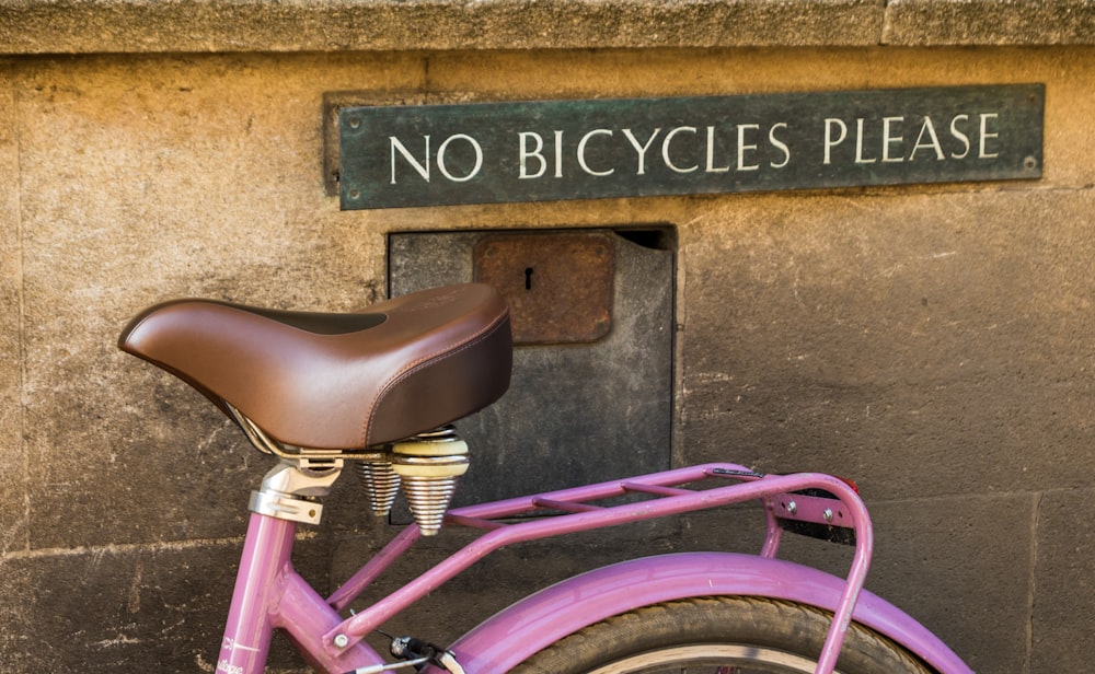 Bicicletta rosa parcheggiata accanto al muro di cemento marrone