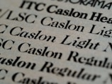 Close-up view of various text samples in different font styles, primarily in black on a light beige background, showcasing typographic details and differences in font weight and style.