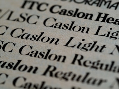 Close-up view of various text samples in different font styles, primarily in black on a light beige background, showcasing typographic details and differences in font weight and style.