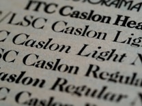 Close-up view of various text samples in different font styles, primarily in black on a light beige background, showcasing typographic details and differences in font weight and style.
