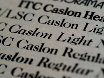 Close-up view of various text samples in different font styles, primarily in black on a light beige background, showcasing typographic details and differences in font weight and style.